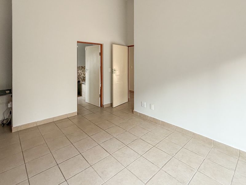An empty bedroom featuring neutral tiled flooring and a built-in wardrobe, with direct access to an adjacent room.