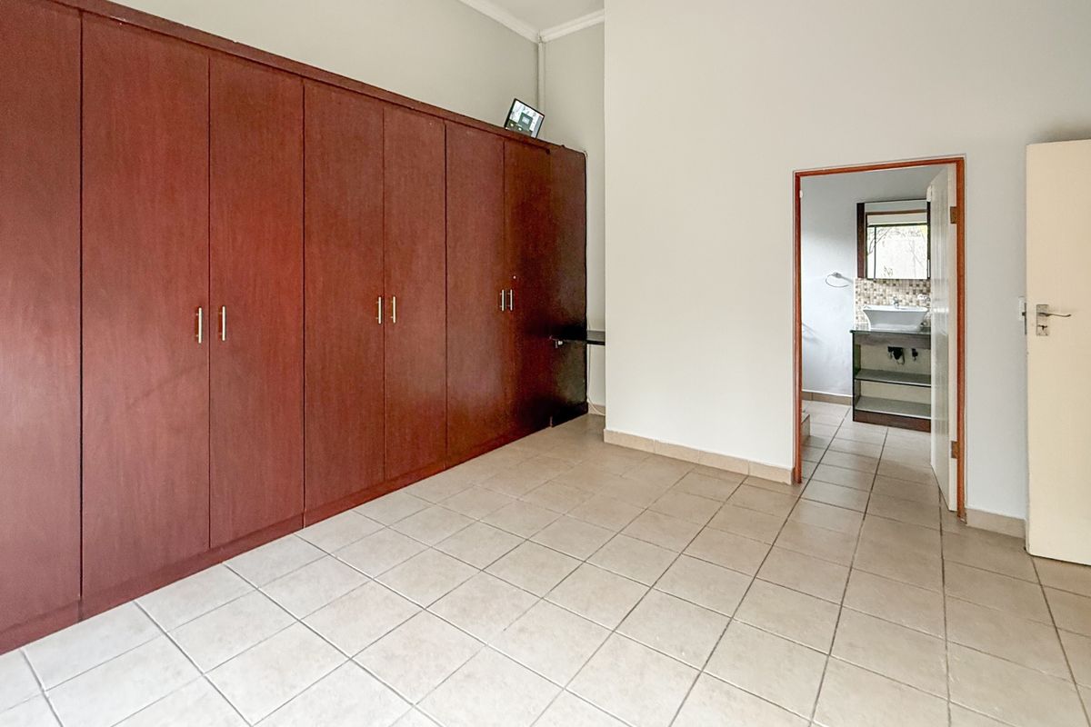 Spacious bedroom featuring extensive built-in wooden cupboards, neutral tiled flooring, and direct access to an en-suite bathroom.