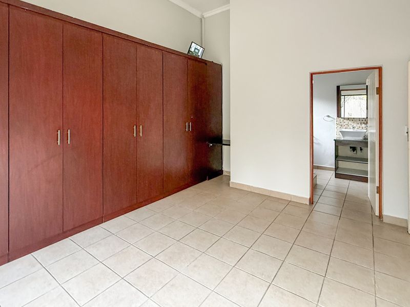 Spacious bedroom featuring extensive built-in wooden cupboards, neutral tiled flooring, and direct access to an en-suite bathroom.