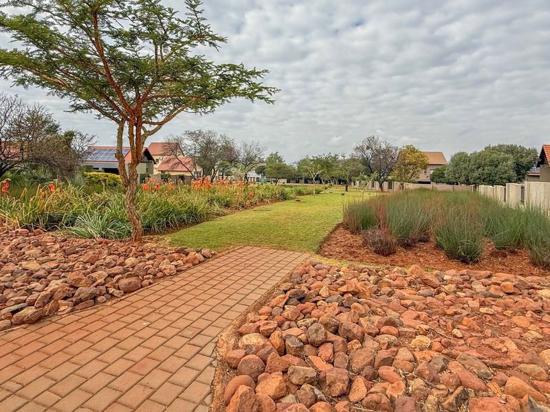 A well-maintained landscaped garden featuring a paved walkway, established trees, and native planting within a residential estate setting.