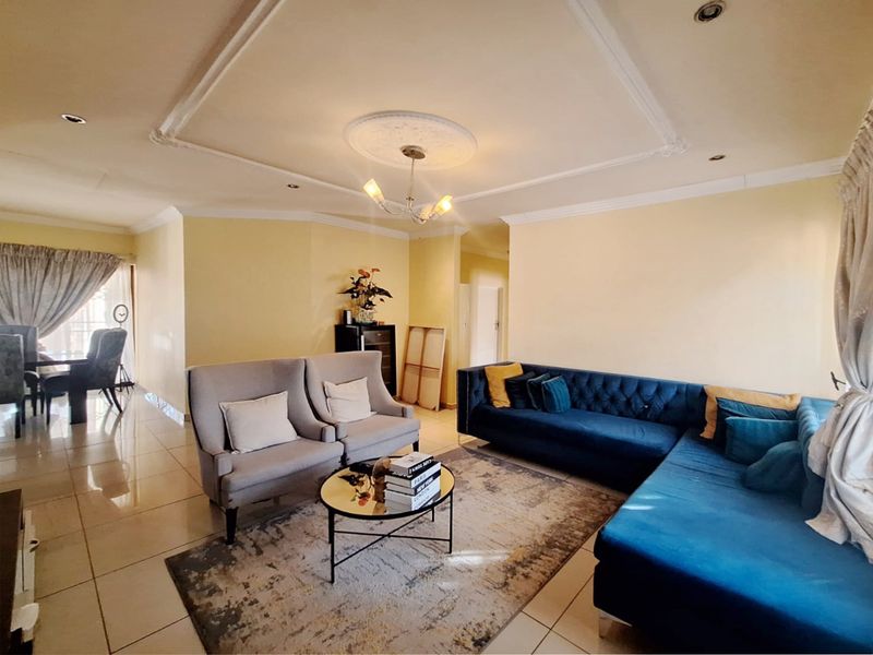 Spacious living room featuring tiled flooring, decorative ceiling detailing with a central rose, and recessed downlighting, creating a bright and comfortable living space.