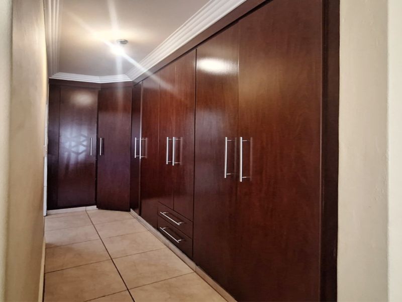 A spacious bedroom area featuring extensive dark wood built-in cupboards, tiled flooring, and decorative coved ceiling detailing.