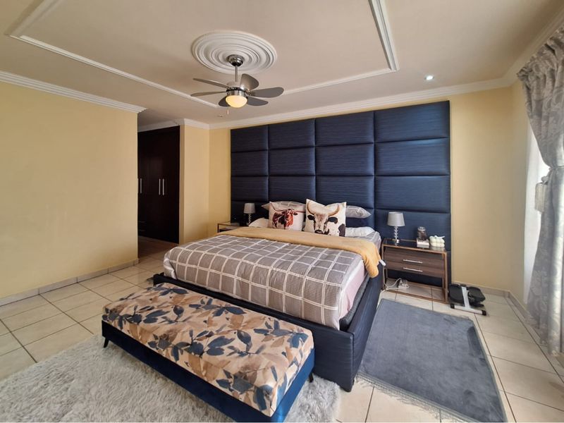 Spacious bedroom featuring a large upholstered headboard, ceiling fan with decorative rose, tiled flooring, and built-in cupboard storage.