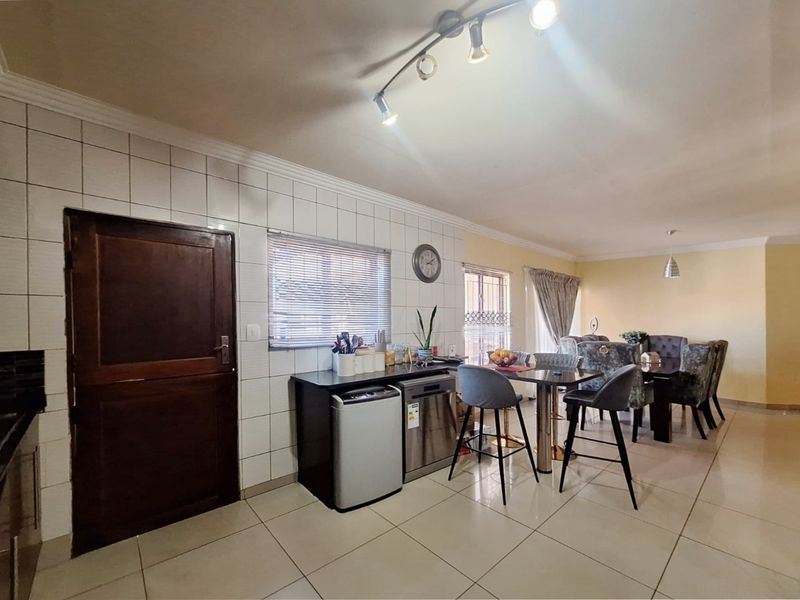 Open-plan living and dining area featuring tiled flooring, track lighting, and built-in kitchen cabinetry with a functional layout.