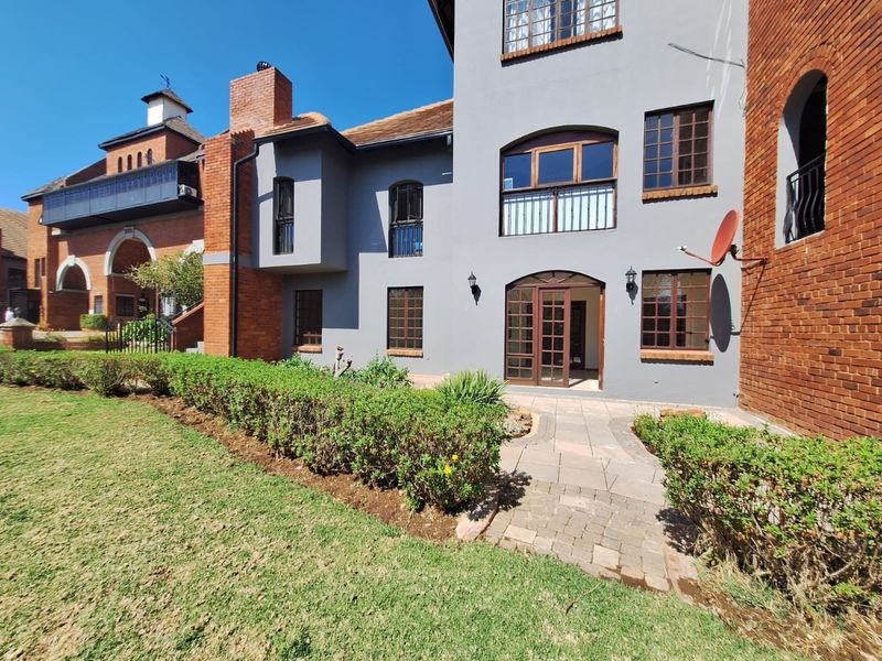 Rear view of a multi-story townhouse featuring a combination of brick and plastered finishes, timber-framed windows, and a paved patio area leading to the garden.