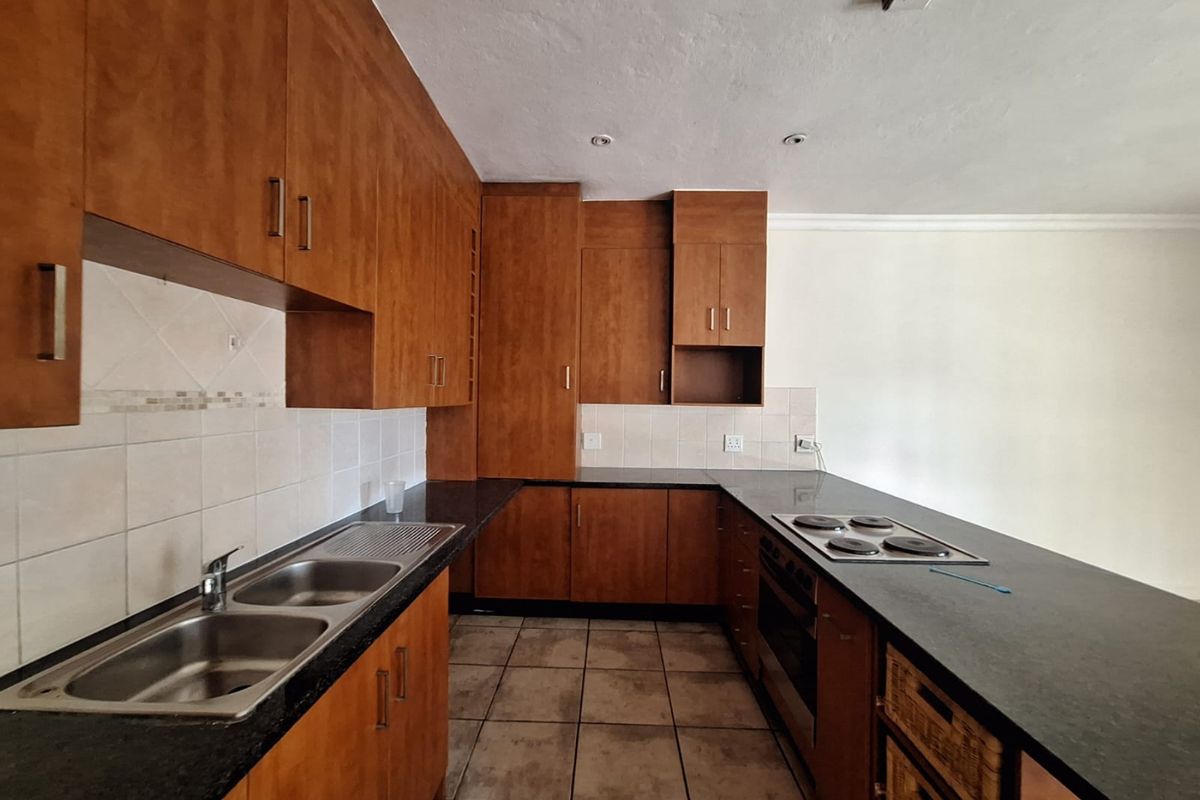 A functional kitchen featuring wooden cabinetry, a double bowl stainless steel sink, built-in oven, electric hob, and tiled flooring.