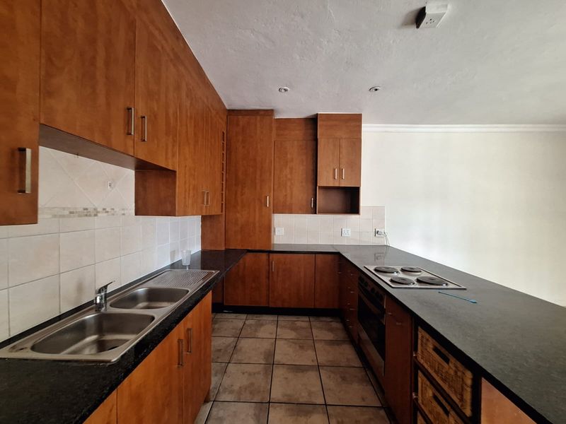 A functional kitchen featuring wooden cabinetry, a double bowl stainless steel sink, built-in oven, electric hob, and tiled flooring.