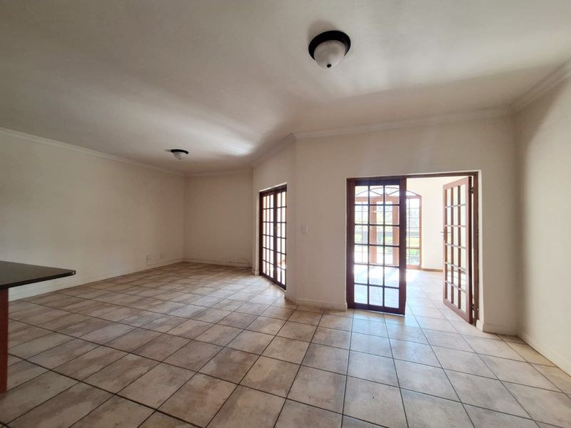 Spacious, empty living area featuring neutral tiled flooring, coving, and multiple sets of wooden-framed French doors providing access to the exterior.