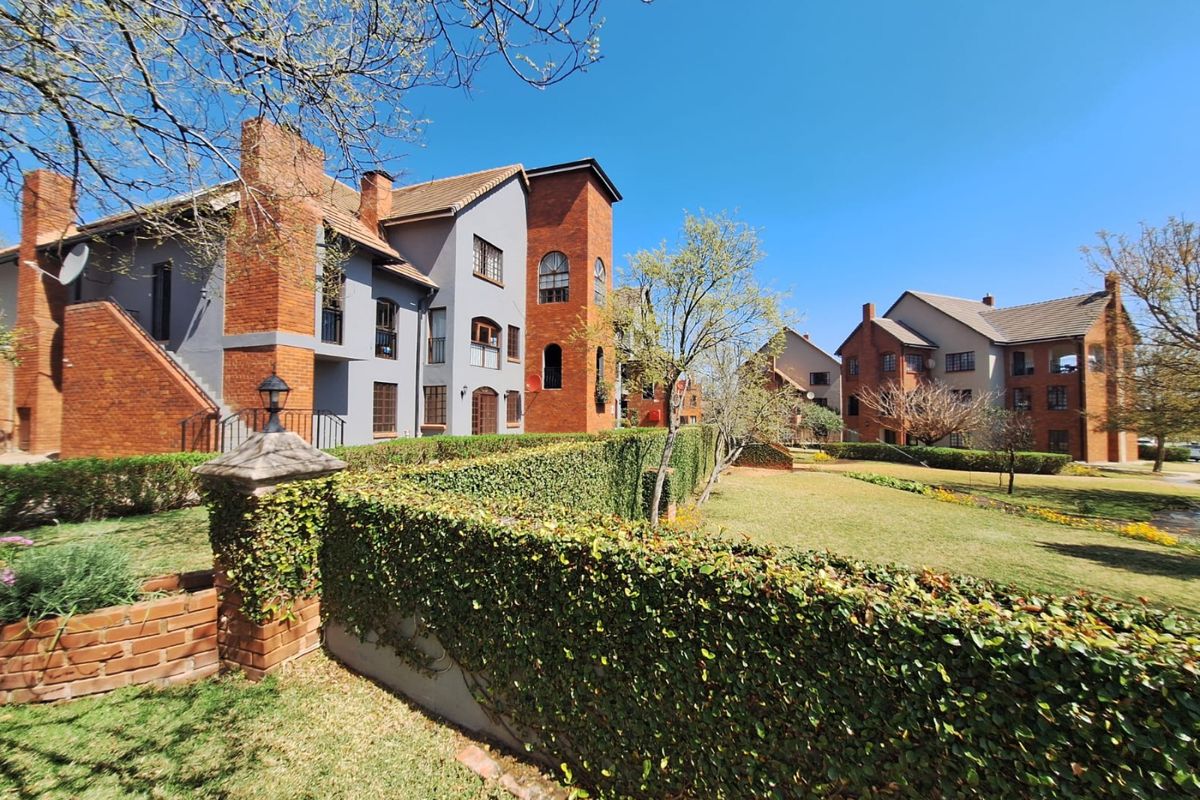 A well-maintained townhouse complex featuring classic brick and plaster architecture, surrounded by manicured gardens and established hedging.