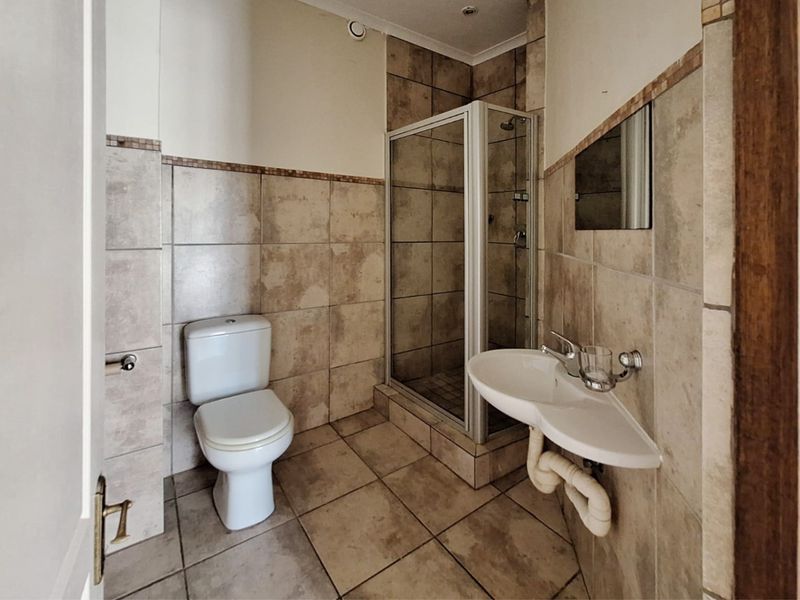 A functional bathroom featuring a corner basin, toilet, and a tiled shower enclosure with neutral wall and floor tiling.