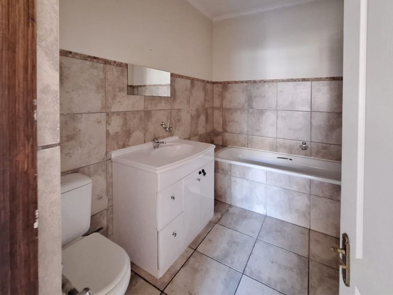 A functional bathroom featuring a vanity cabinet, bathtub, and toilet with neutral wall and floor tiling throughout.