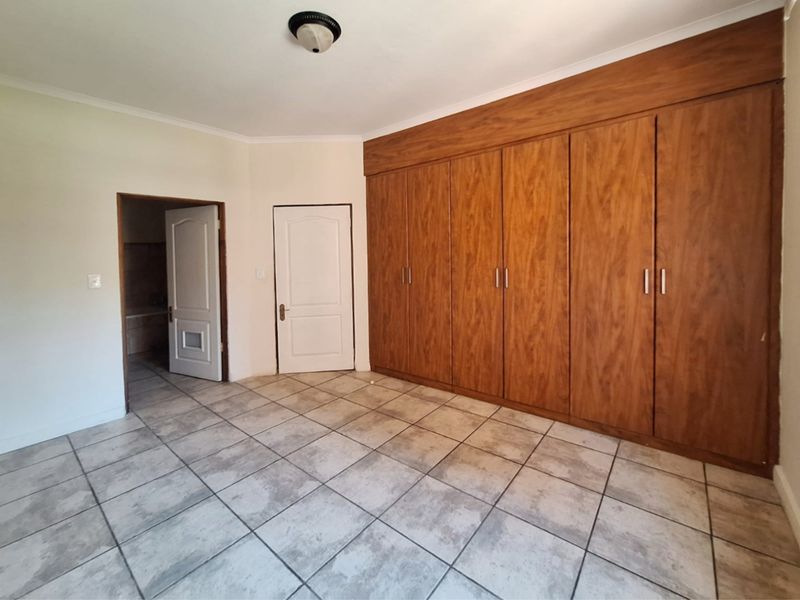 A spacious, empty bedroom featuring extensive built-in wooden cupboards, tiled flooring, and direct access to an adjoining room.