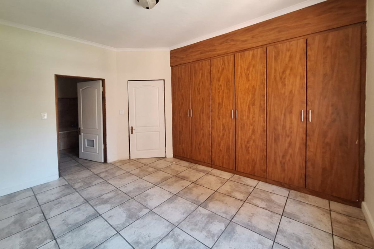 A spacious, empty bedroom featuring extensive built-in wooden cupboards, tiled flooring, and direct access to an adjoining room.
