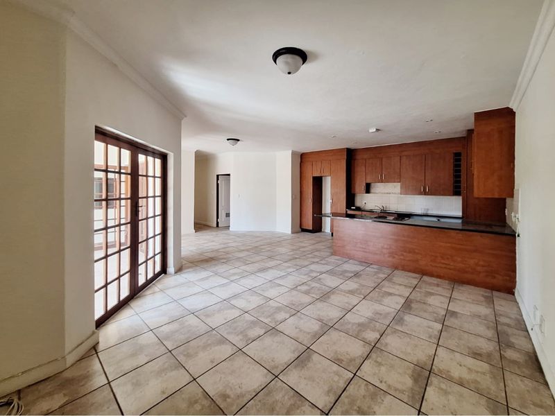 Spacious open-plan living and kitchen area featuring wooden cabinetry, granite countertops, tiled flooring, and direct access to the patio through french doors.