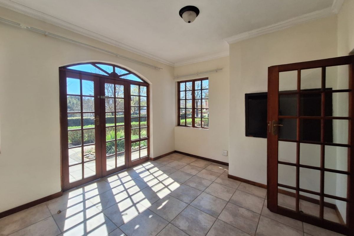 A bright, empty living area featuring tiled flooring, timber-framed windows, and classic french doors leading to the garden.