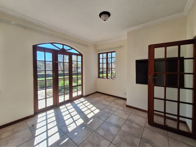 A bright, empty living area featuring tiled flooring, timber-framed windows, and classic french doors leading to the garden.