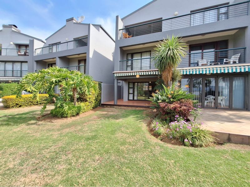 Rear view of a multi-story townhouse featuring a covered patio, upper-level balconies with metal railings, and a well-maintained landscaped garden.