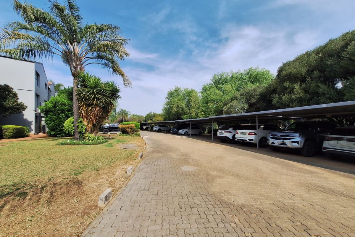 A well-maintained townhouse complex parking area featuring covered carports, paved driveway, and established garden landscaping.