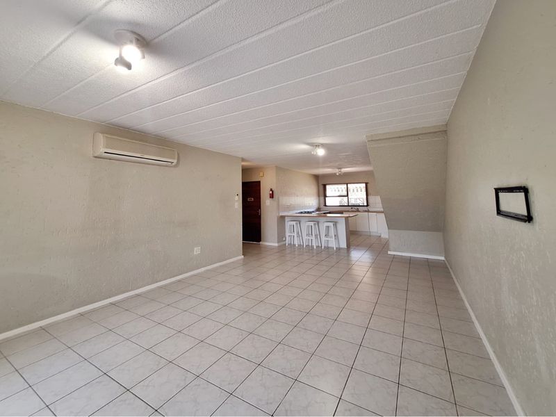 Spacious open-plan living and kitchen area featuring tiled flooring, a breakfast bar, and a wall-mounted air conditioning unit.