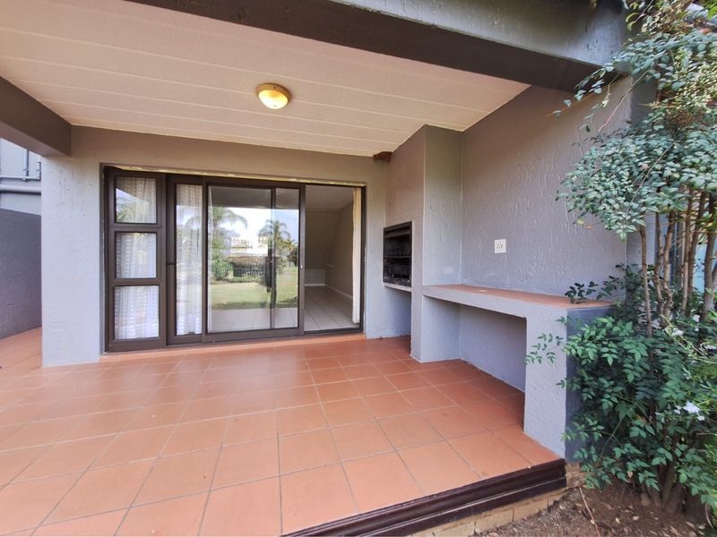 Covered patio featuring tiled flooring, a built-in braai, and a fixed counter, providing direct access to the interior through sliding glass doors.