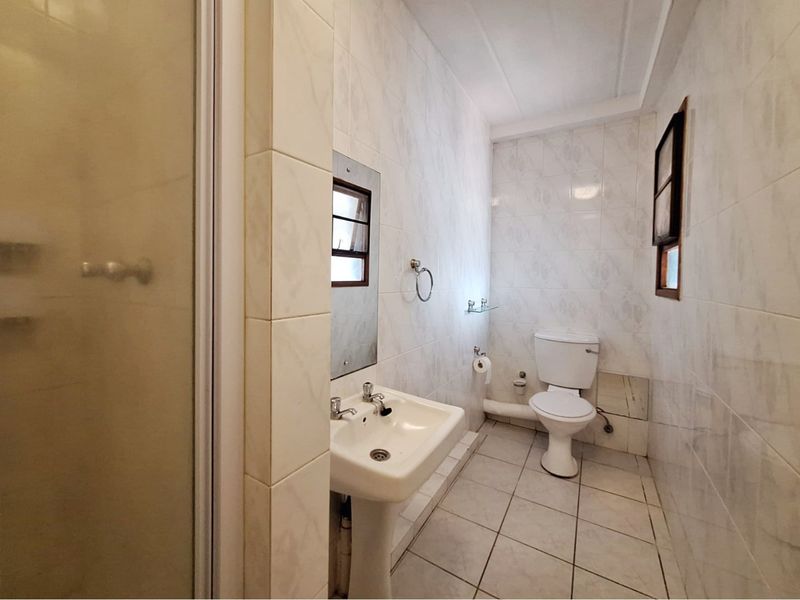 A functional bathroom featuring a pedestal basin, toilet, and shower enclosure with fully tiled walls and flooring, requiring some cosmetic updates.