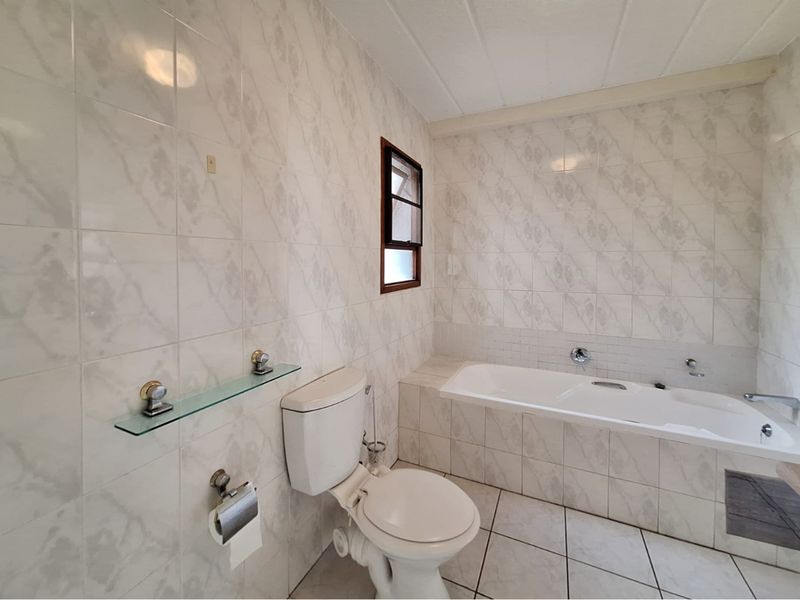 A functional bathroom featuring a built-in bathtub, toilet, and fully tiled walls and floors, offering a clean, neutral canvas for potential updates.