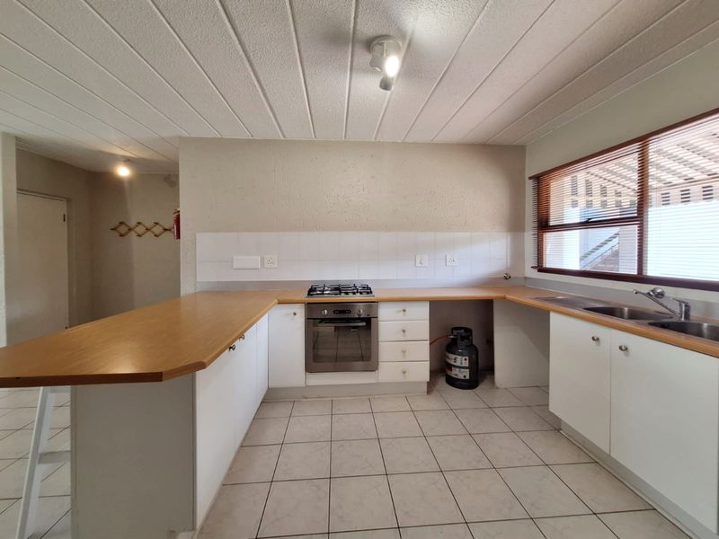 A functional kitchen featuring white cabinetry, laminate countertops, a built-in oven with gas hob, and tiled flooring, offering a clean and practical workspace.