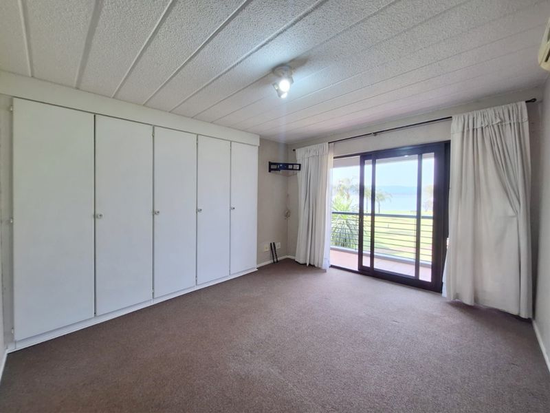 Spacious bedroom featuring extensive built-in cupboards, carpeted flooring, and sliding glass doors providing direct access to a balcony with scenic views.
