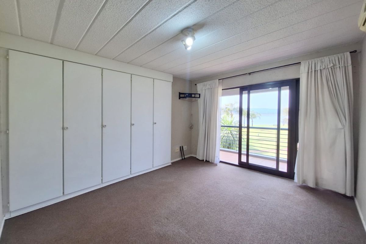 Spacious bedroom featuring extensive built-in cupboards, carpeted flooring, and sliding glass doors providing direct access to a balcony with scenic views.