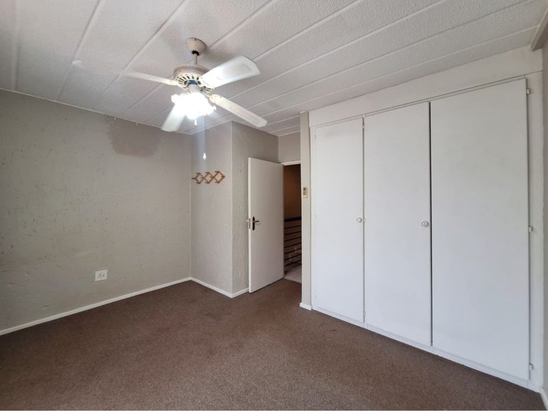 An empty bedroom featuring built-in cupboards, a ceiling fan, and carpeted flooring, requiring cosmetic updates to the walls and flooring.