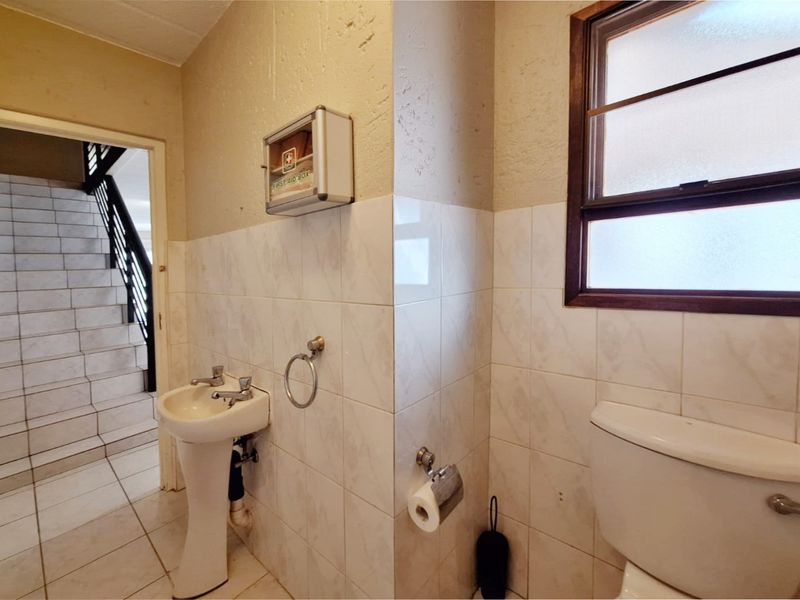 A compact bathroom featuring a pedestal basin, toilet, and tiled finishes, with a view into the adjacent stairwell area.