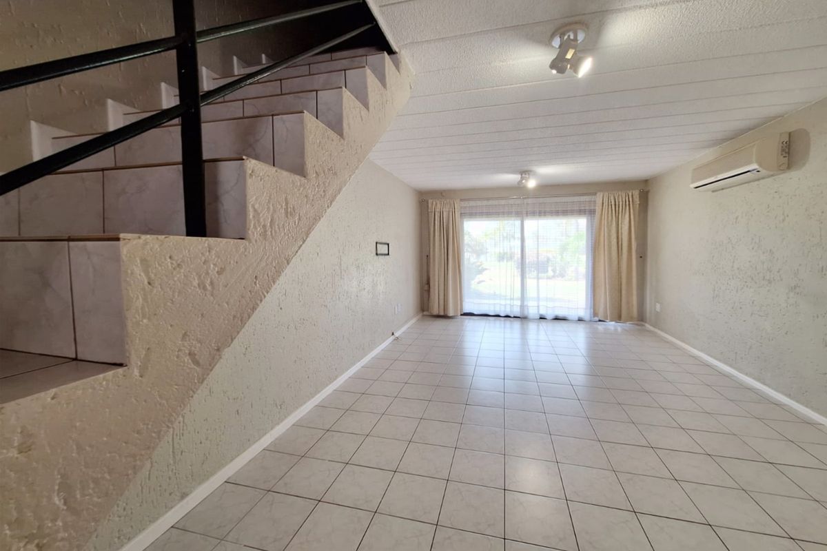 Spacious open-plan living area featuring ceramic floor tiles, a staircase with a metal handrail, and a sliding glass door leading to the exterior.