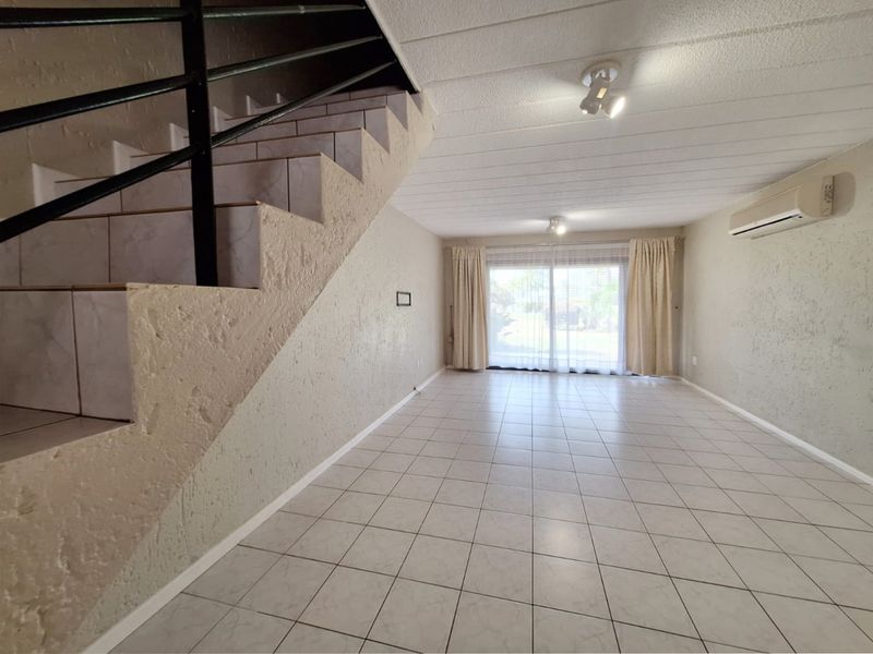 Spacious open-plan living area featuring ceramic floor tiles, a staircase with a metal handrail, and a sliding glass door leading to the exterior.