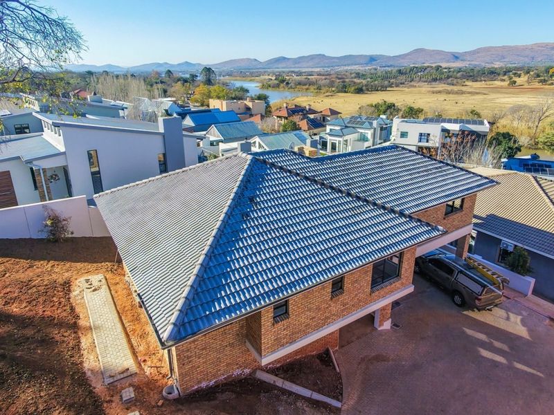 Aerial view of a modern face brick house with a tiled roof, featuring a paved driveway and scenic landscape views in a residential estate.