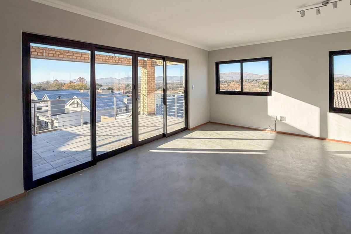 Spacious, light-filled living area featuring polished concrete floors, large sliding doors opening to a balcony, and expansive views of the surrounding landscape.