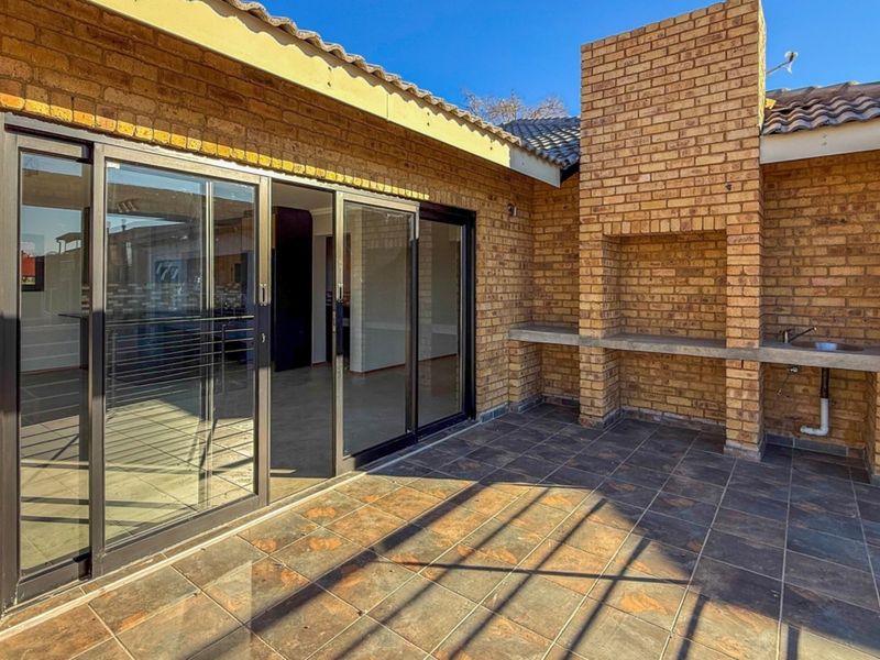 Covered patio featuring a built-in brick braai, concrete prep area, tiled flooring, and large sliding glass doors providing access to the interior.