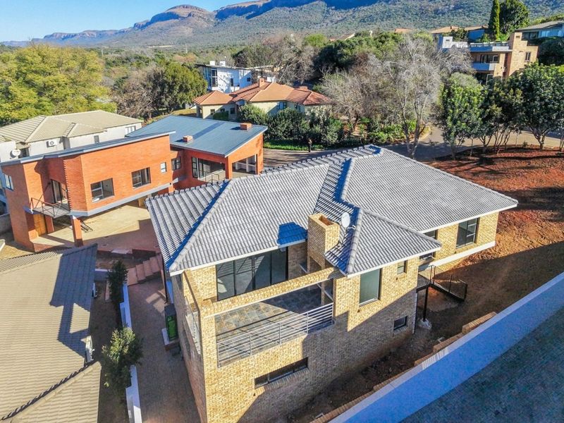 Aerial view of a multi-level brick residential property featuring a tiled roof, balcony, and paved driveway within a suburban estate setting.