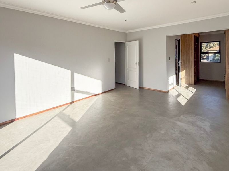 Spacious bedroom featuring polished concrete flooring, built-in cupboards, and a ceiling fan, offering a clean and modern blank canvas.