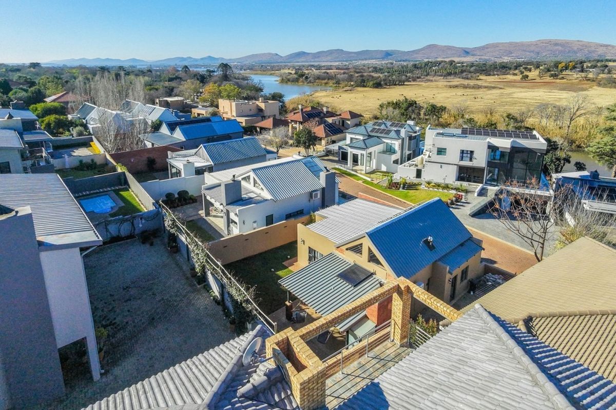 Aerial view of a residential estate featuring modern homes with metal roofs, solar installations, and scenic river views in the background.