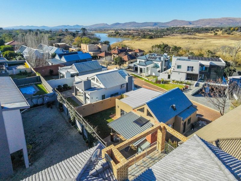 Aerial view of a residential estate featuring modern homes with metal roofs, solar installations, and scenic river views in the background.