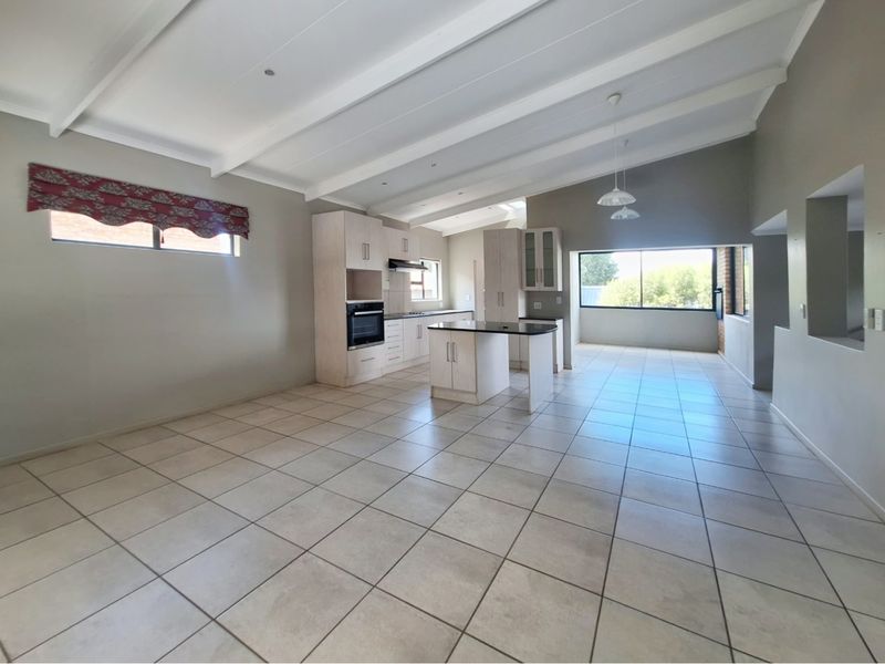 Spacious open-plan living and kitchen area featuring tiled floors, exposed beam ceilings, and a functional kitchen island with built-in appliances.