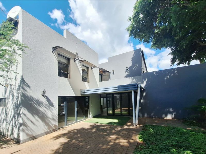 Rear view of the townhouse featuring a paved patio area, covered outdoor space, and modern aluminium sliding doors leading into the home.