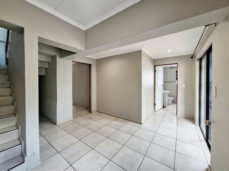 A bright, tiled hallway featuring a staircase and access to an adjacent bathroom, offering a clean and neutral foundation for interior design.