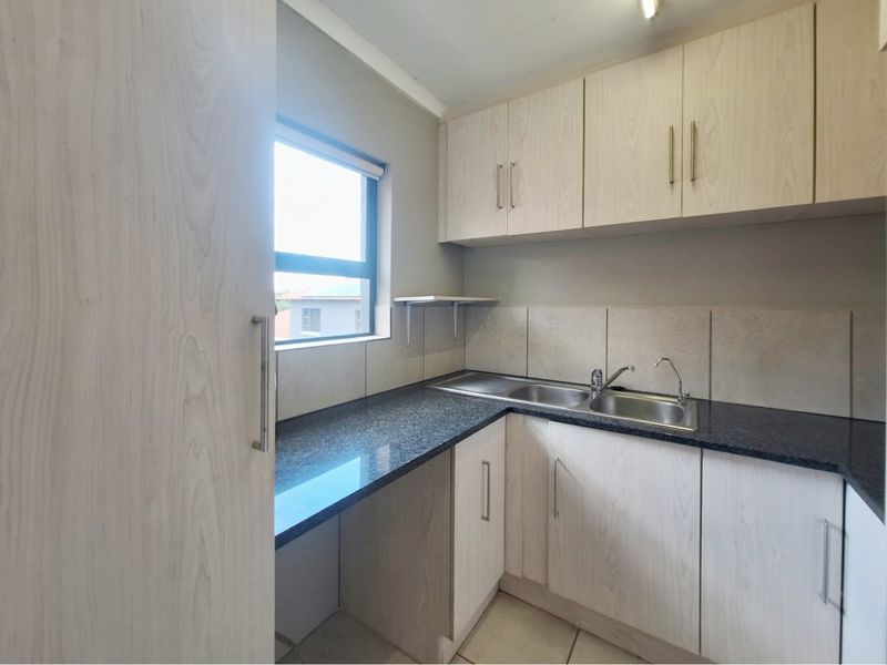 A functional scullery featuring light wood-look cabinetry, granite countertops, and a stainless steel double sink with a tiled backsplash.