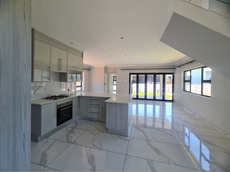 Modern open-plan kitchen and living area featuring sleek cabinetry, stone countertops, high-gloss marble-look floor tiles, and large aluminium stacker doors leading to the garden.