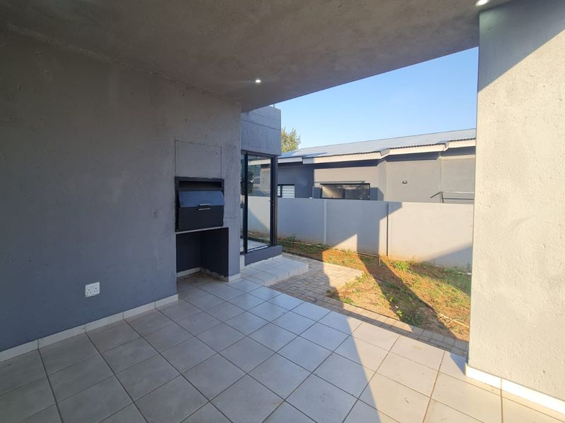 A covered patio area featuring a built-in braai, tiled flooring, and recessed lighting, overlooking a private backyard with a concrete boundary wall.