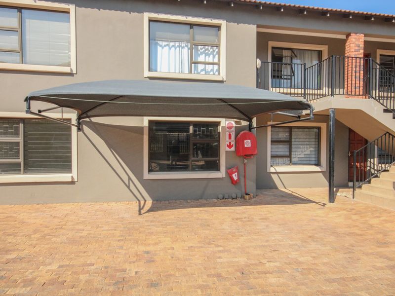 Exterior view of an apartment building featuring a paved parking area with a shade sail, fire safety equipment, and an external staircase.