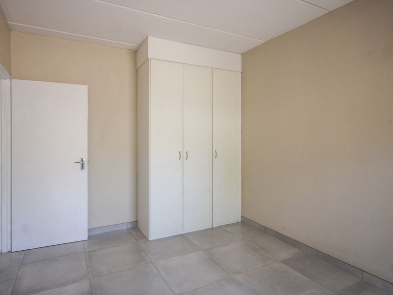 A clean, empty bedroom featuring neutral wall tones, large format floor tiles, and a functional built-in wardrobe.
