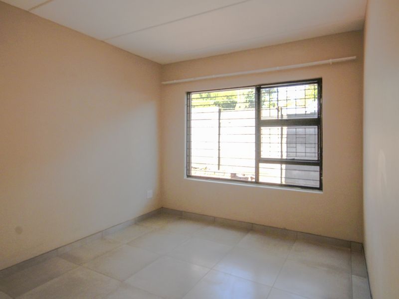 An empty bedroom featuring neutral wall paint, tiled flooring, and a window fitted with security bars and a curtain rail.