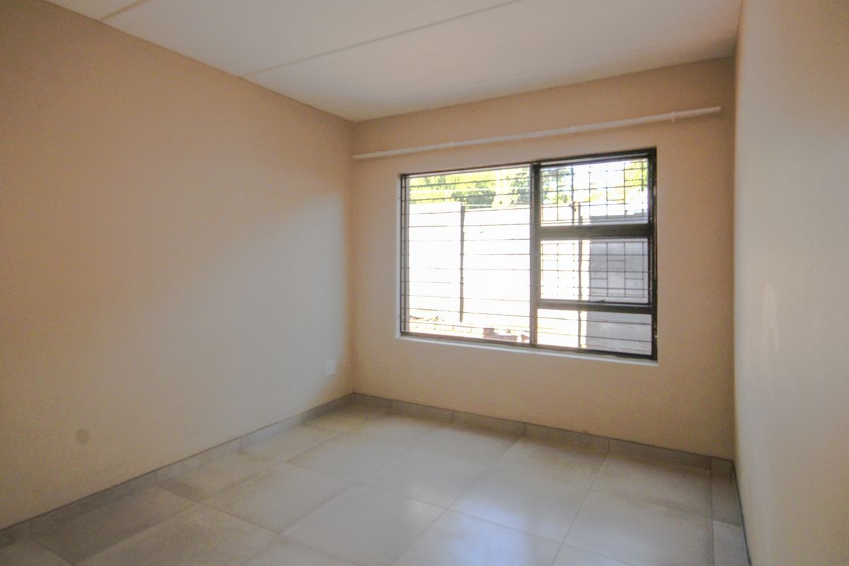 An empty bedroom featuring neutral wall paint, tiled flooring, and a window fitted with security bars and a curtain rail.